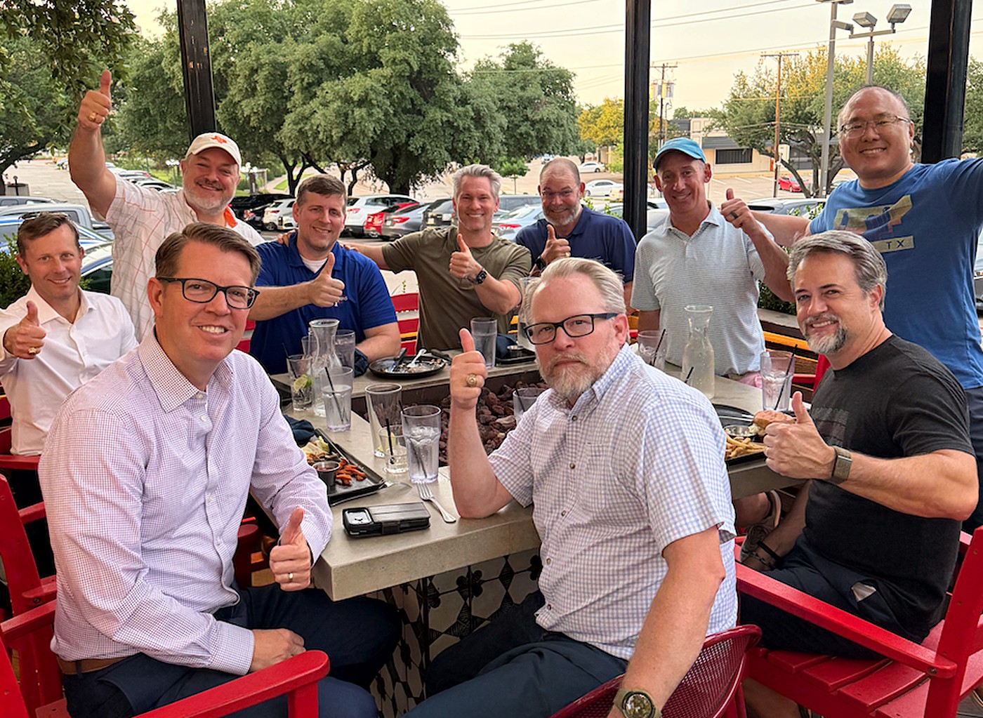 Ten BYX alumni around a patio table on a summer evening, all giving a thumbs up