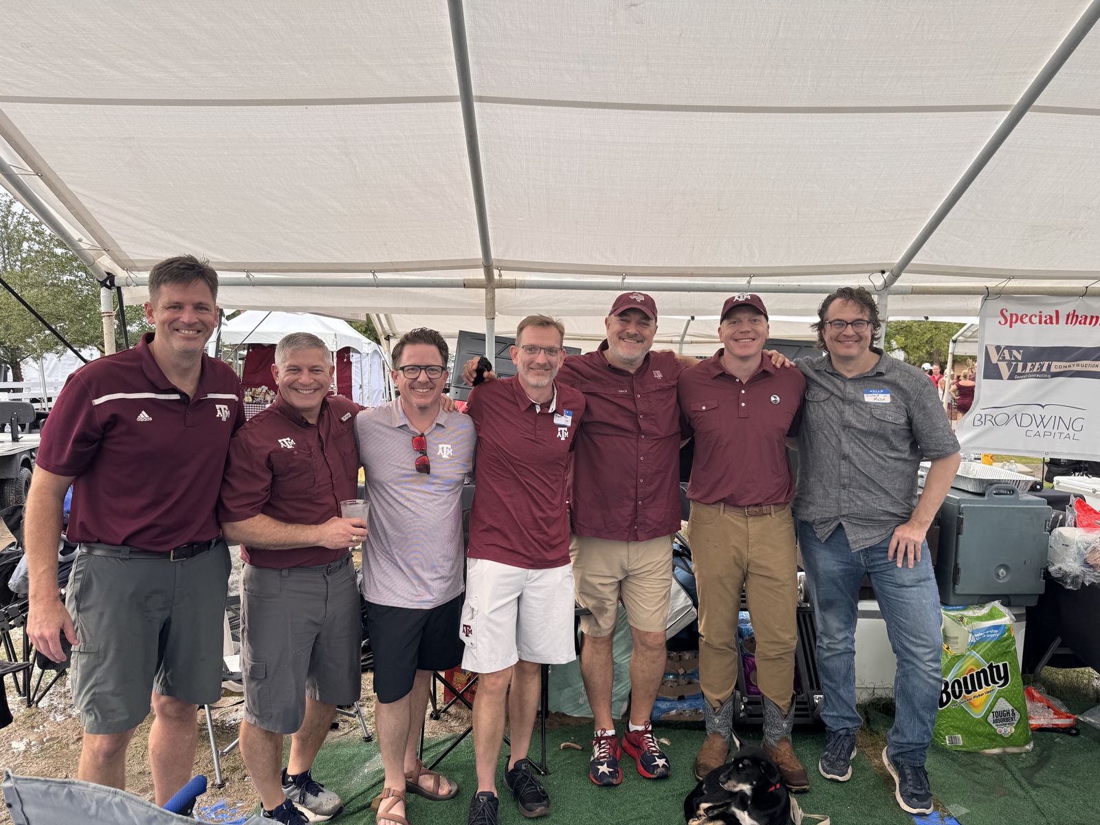 Seven BYX alumni standing under the tent in front of the sponsor banner