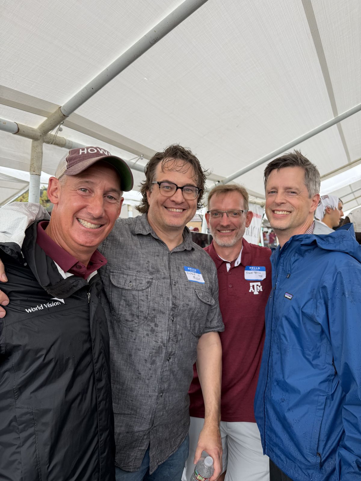 Four alumni with name tags smiling under the tent